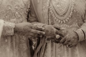 Close up of hands exchanging wedding rings during a traditional ceremony with intricate henna designs.