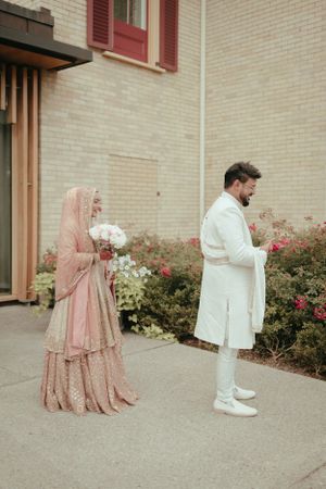 A wedding couple in coordinated white and pink outfits standing apart for a portrait.