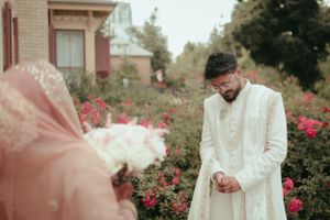 A wedding couple sharing a moment in a rose garden wearing traditional South Asian attire.