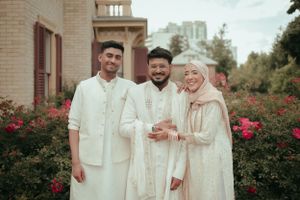 Group in traditional white and cream attire pose together in front of rose garden.