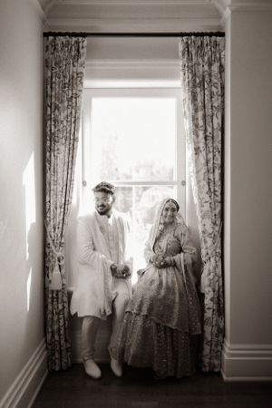 Black and white portrait of couple in traditional wedding attire framed by elegant doorway.