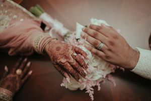 Close-up shot of hands with intricate henna design touching white fabric in a wedding ceremony.