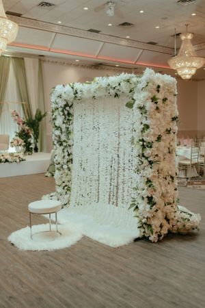 Elegant white floral wedding backdrop with cascading flowers and crystal curtains in a reception hall.