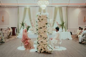 Elegant white floral wedding cake display in grand reception hall with draped curtains.