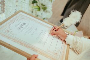 Close up of hands signing a wedding certificate with an elegant white feather pen.