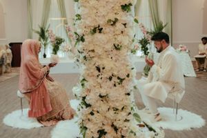 Intimate wedding ceremony moment with floral wall backdrop and white chairs.