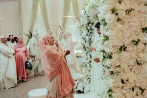 Wedding celebration in elegant hall with white floral arrangements and guests in traditional attire.