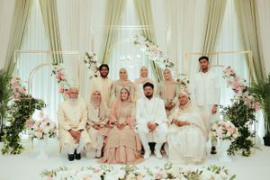 Formal wedding group portrait with floral arch backdrop in traditional South Asian attire.