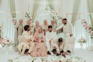 Wedding party in coordinated formal attire poses on decorative stage with floral arch and soft lighting.