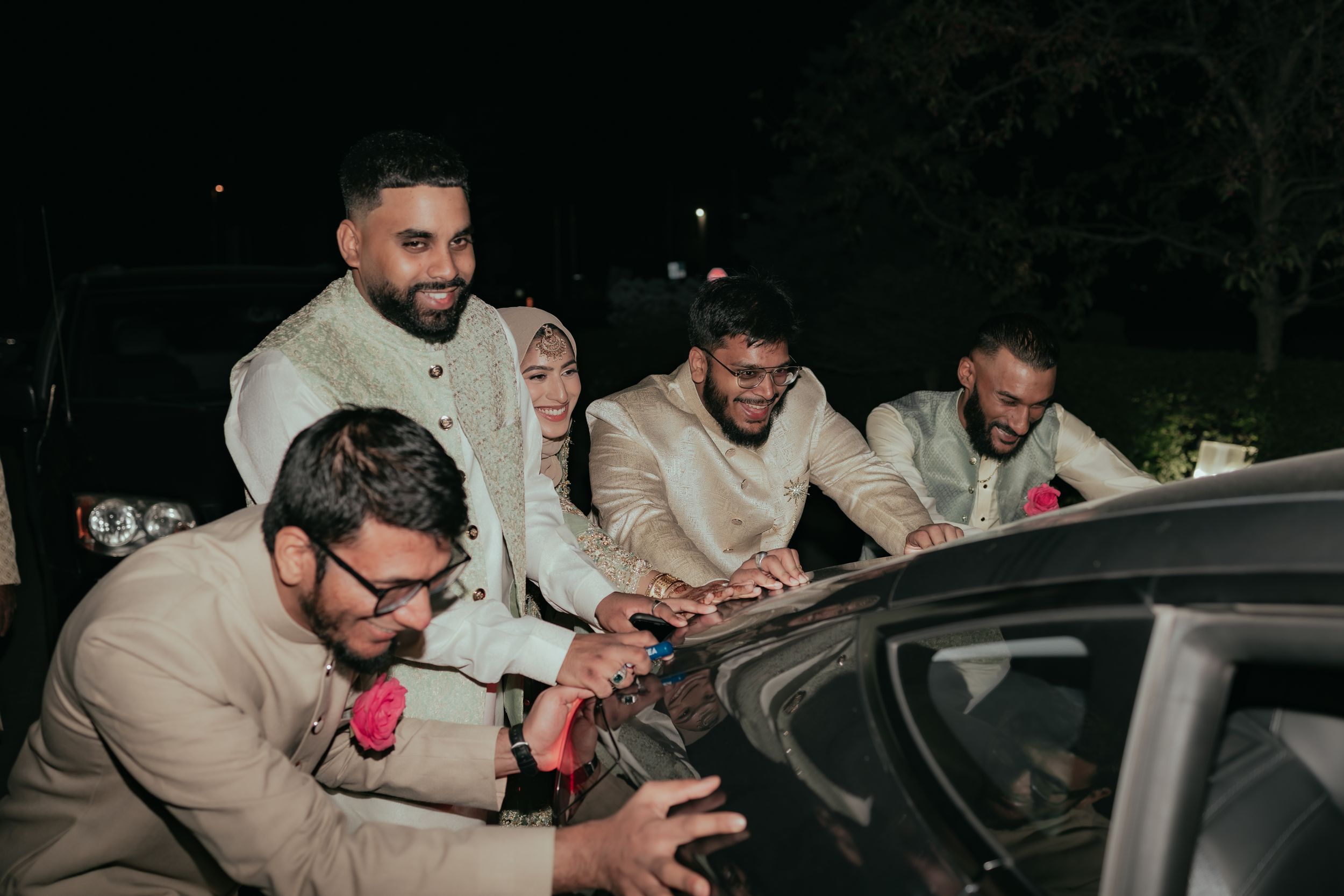 Group in formal attire gathered around car during nighttime celebration.