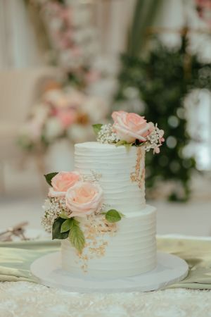 Elegant white wedding cake decorated with fresh pink roses and delicate green foliage.