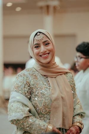 Person in formal hijab and embellished dress at elegant indoor celebration.