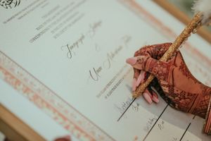 Hand adorned with traditional henna designs signing an official document with a gold pen.