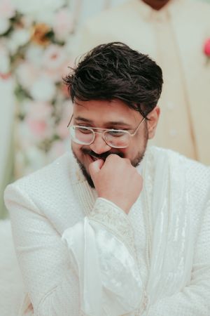 Person in white embroidered attire smiling shyly during a wedding ceremony.