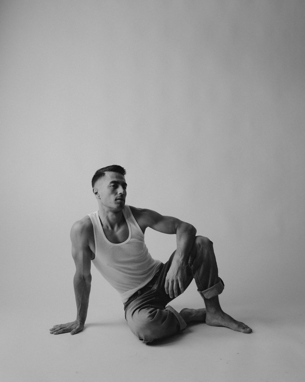 Artistic portrait of athletic figure in white tank top and cargo pants on white background.