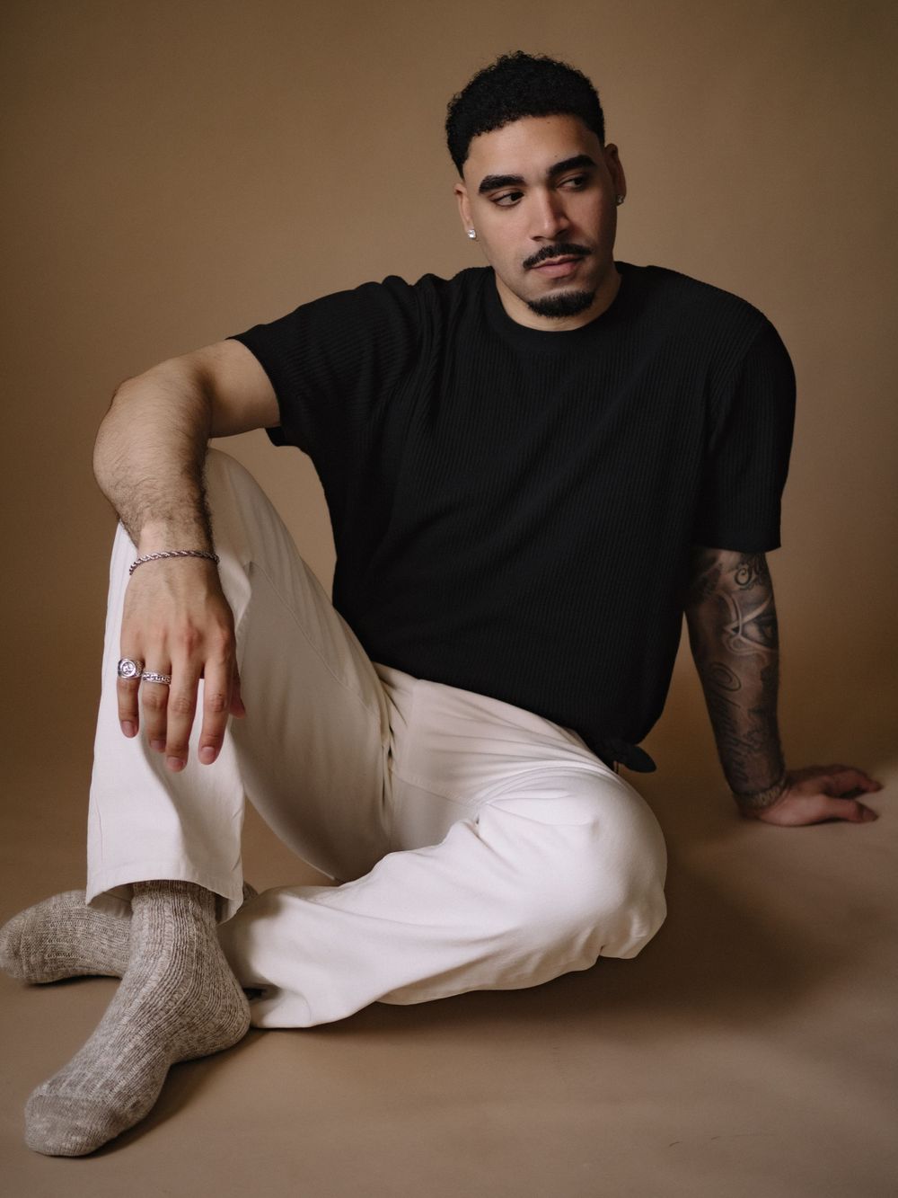 Studio portrait of model in black t-shirt and white pants posing against brown background.