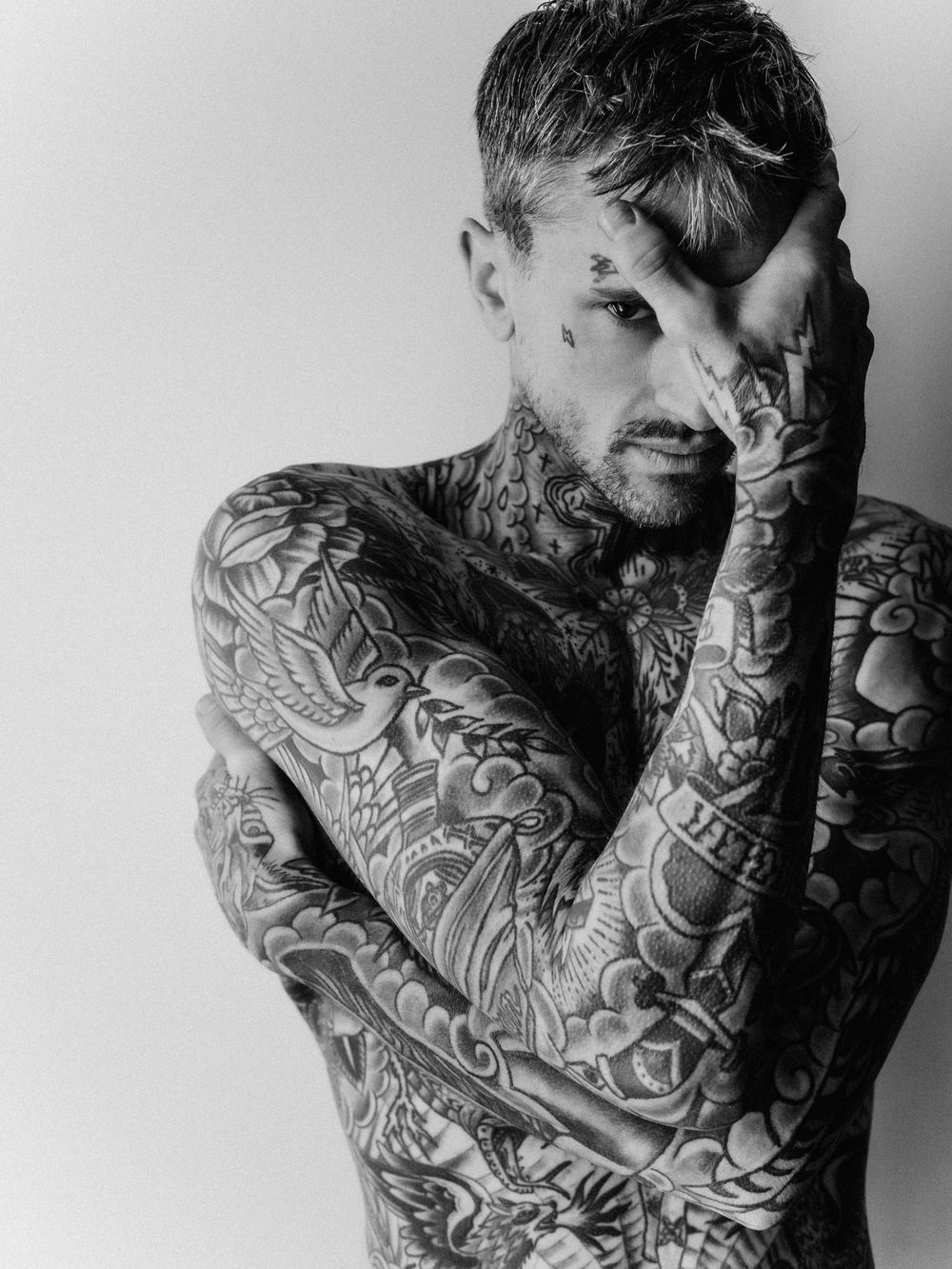 Black and white artistic portrait showing heavily tattooed person with intricate body art covering their torso and arms.