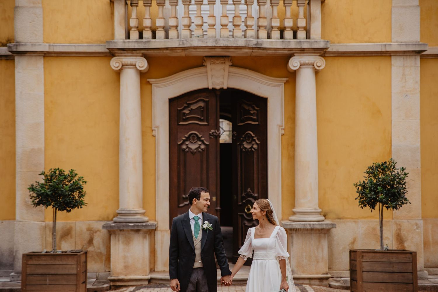 Elegant yellow stone building facade with classical columns frames a wedding scene.