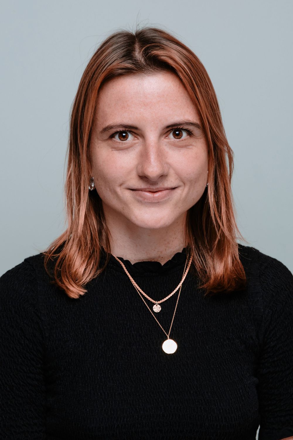 A sequence of five headshots showing a person with red hair wearing a black top and necklace against a gray background.