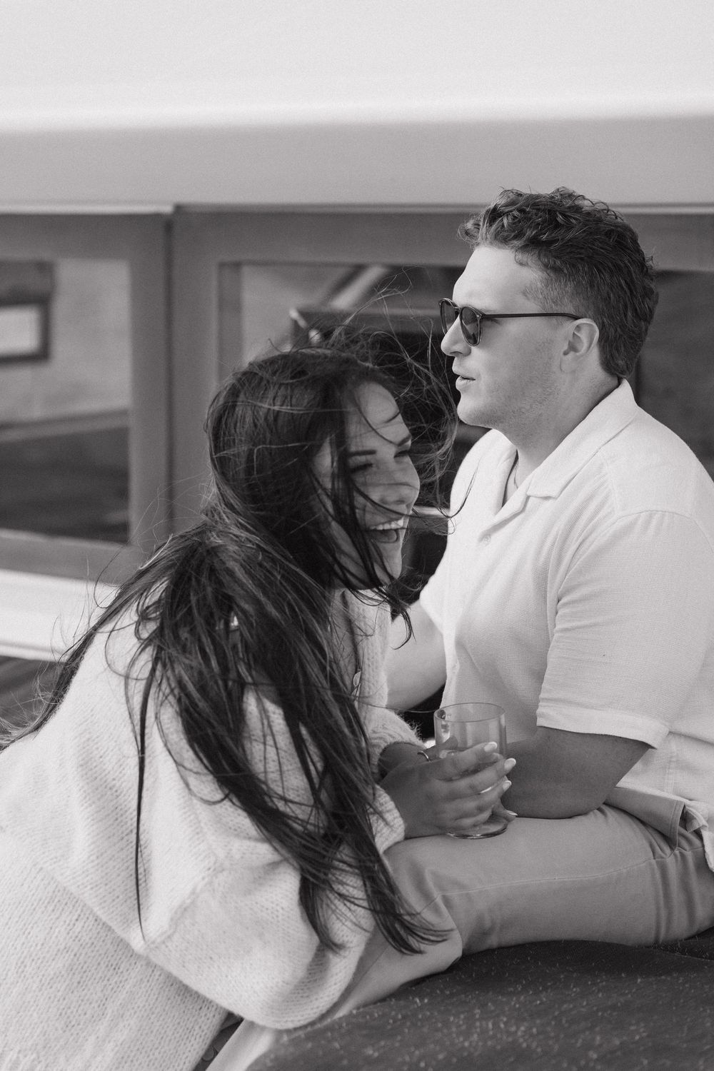 Black and white photo of a laughing couple sitting close together on a sailboat on a windy day in the Halifax harbour.