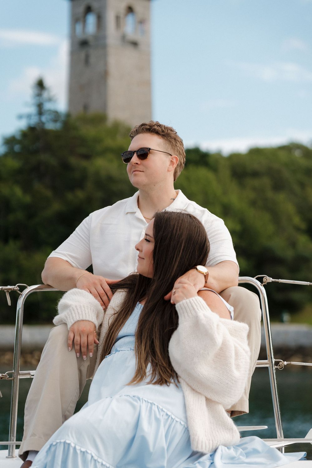 Couple relaxing on a sailboat with the Halifax Dingle Tower and green trees in the background.
