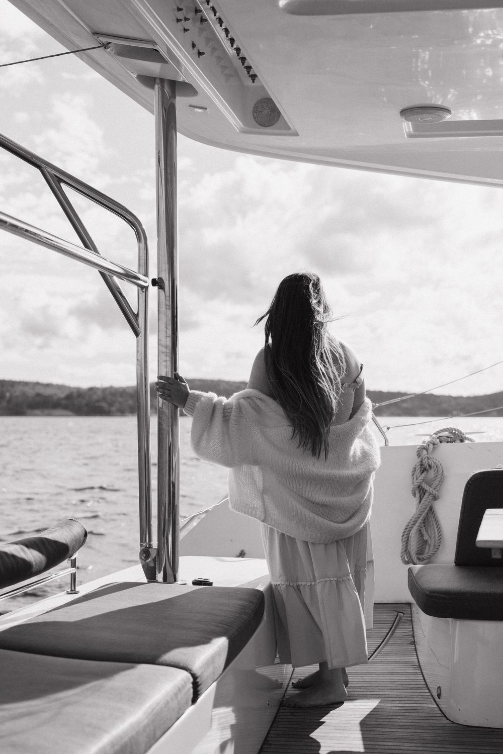 Black and white photo of a woman in a white robe standing on a yacht deck gazing at the open water.