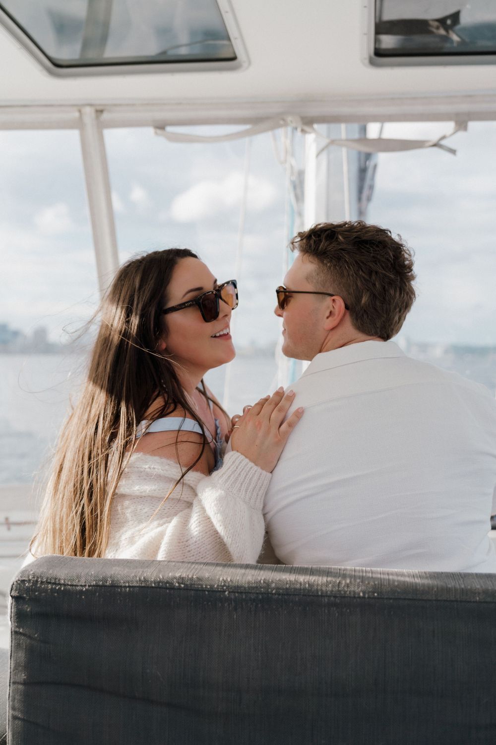 Romantic couple in sunglasses smiling at each other while seated on a yacht on a sunny day in Halifax Habour.