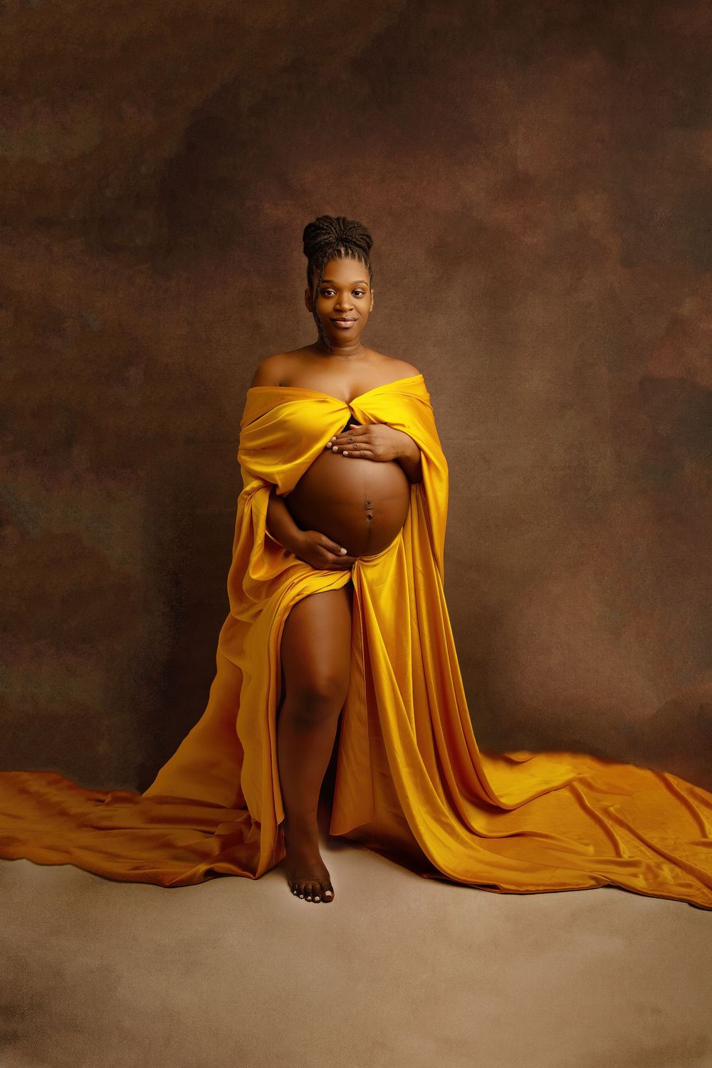 Dramatic maternity portrait with woman in flowing yellow dress against dark background.