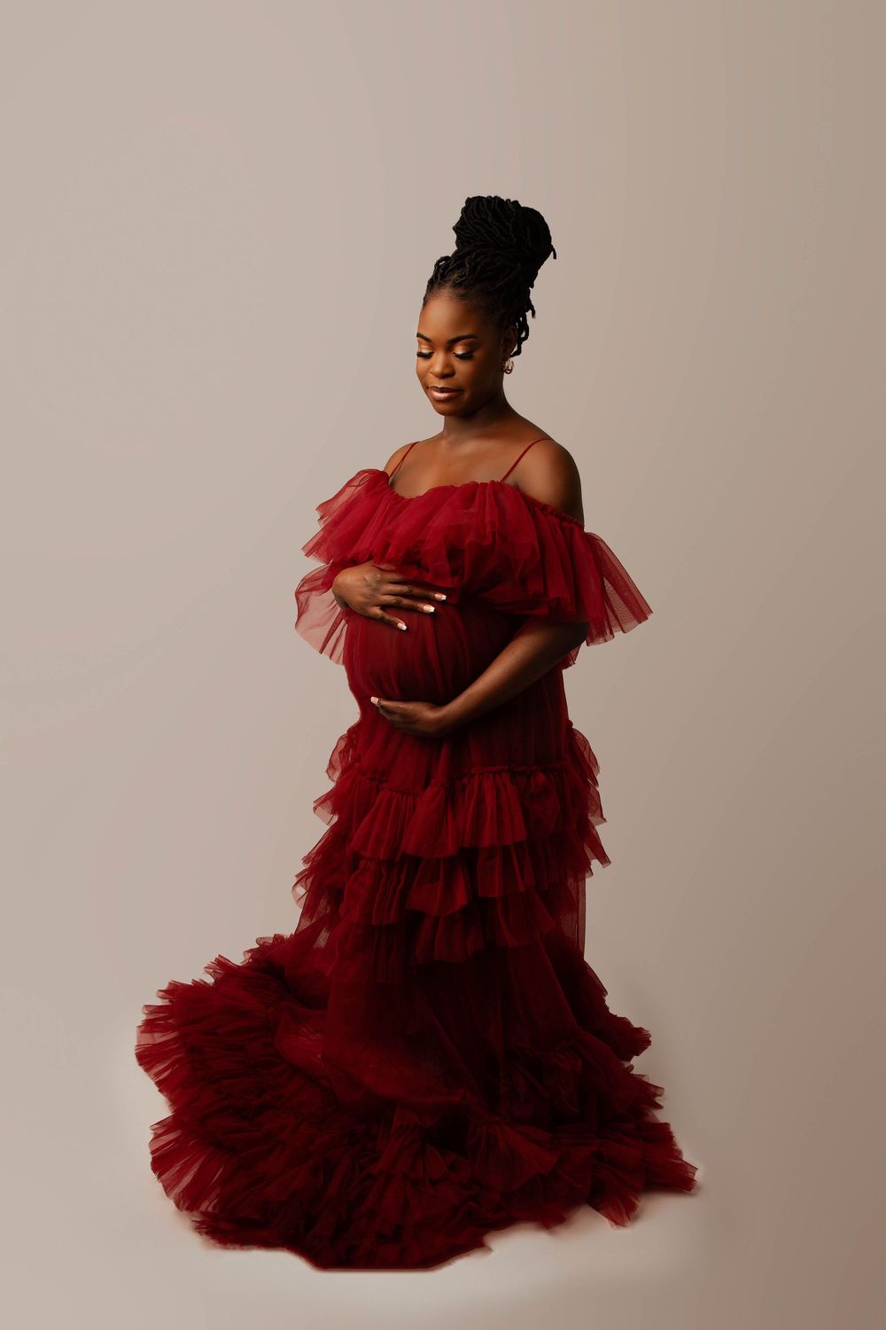Elegant maternity portrait in flowing red tulle gown against neutral backdrop.