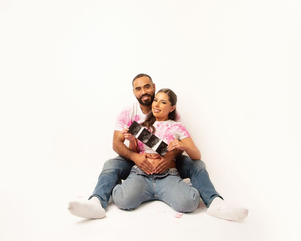 Couple sitting together holding ultrasound photos in casual attire.