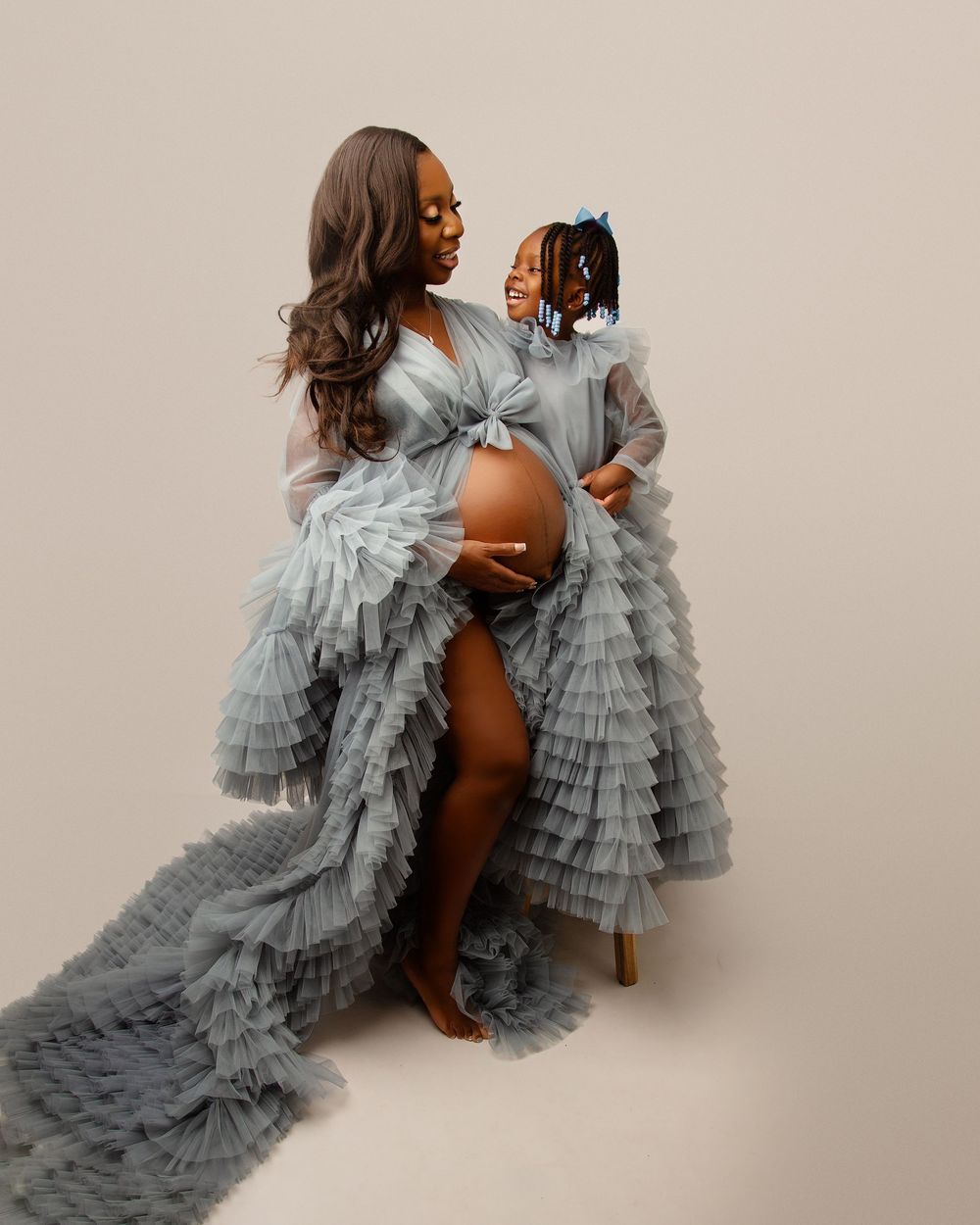 Mother and child wearing matching grey tulle dresses in elegant maternity portrait.