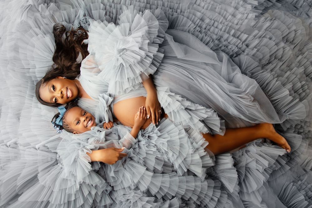 Maternity photoshoot featuring two people laying on grey tulle fabric.