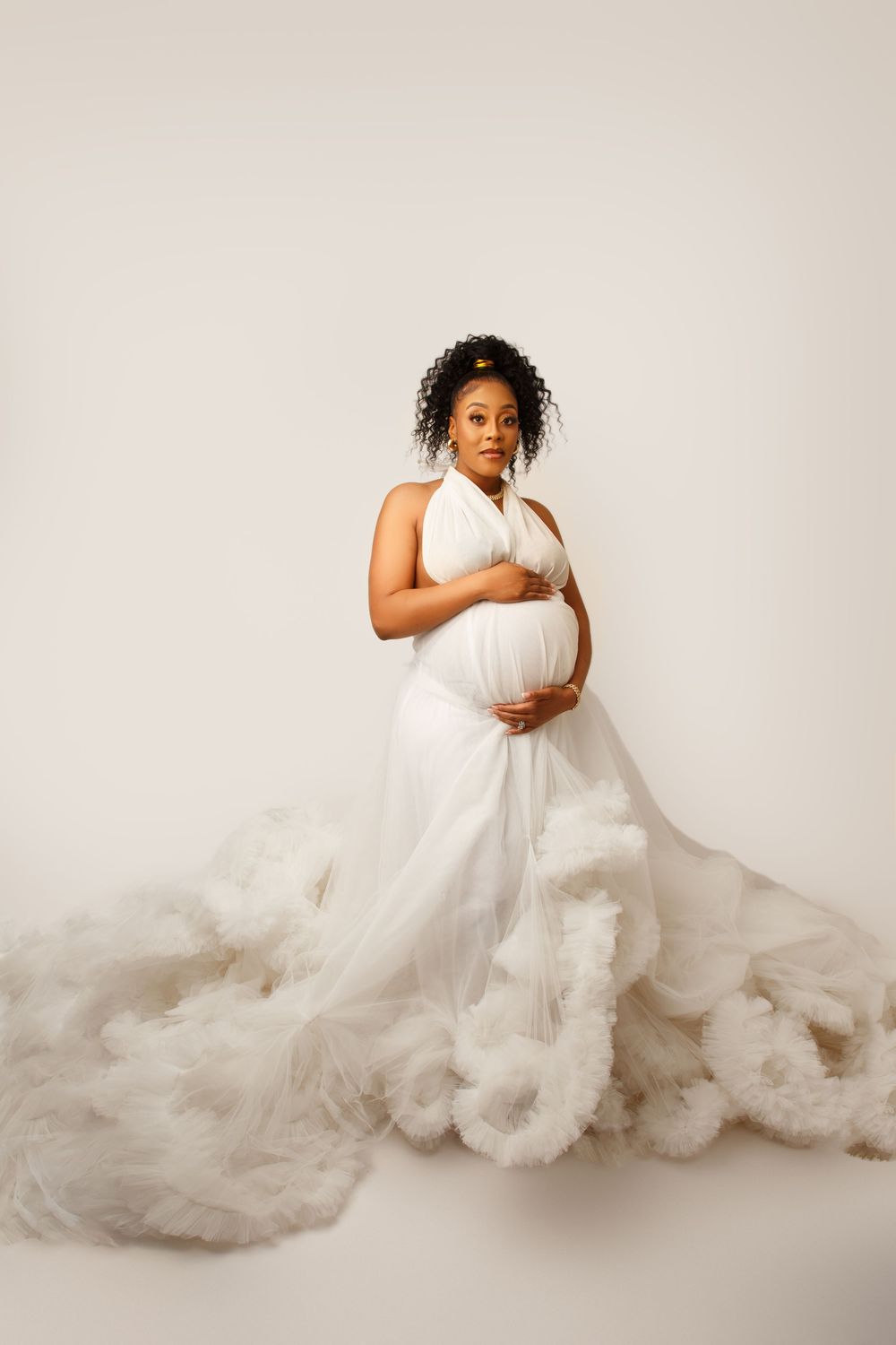 Dramatic maternity portrait in flowing white gown against neutral background.