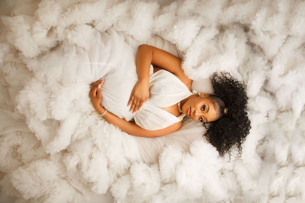 Person in white dress lying on soft white textured background in artistic pose.