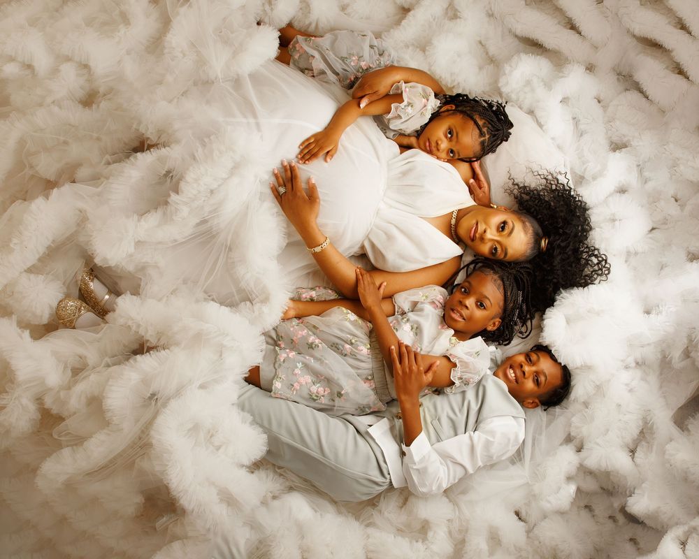 Four people lying together on white fluffy bedding in a tender family portrait.