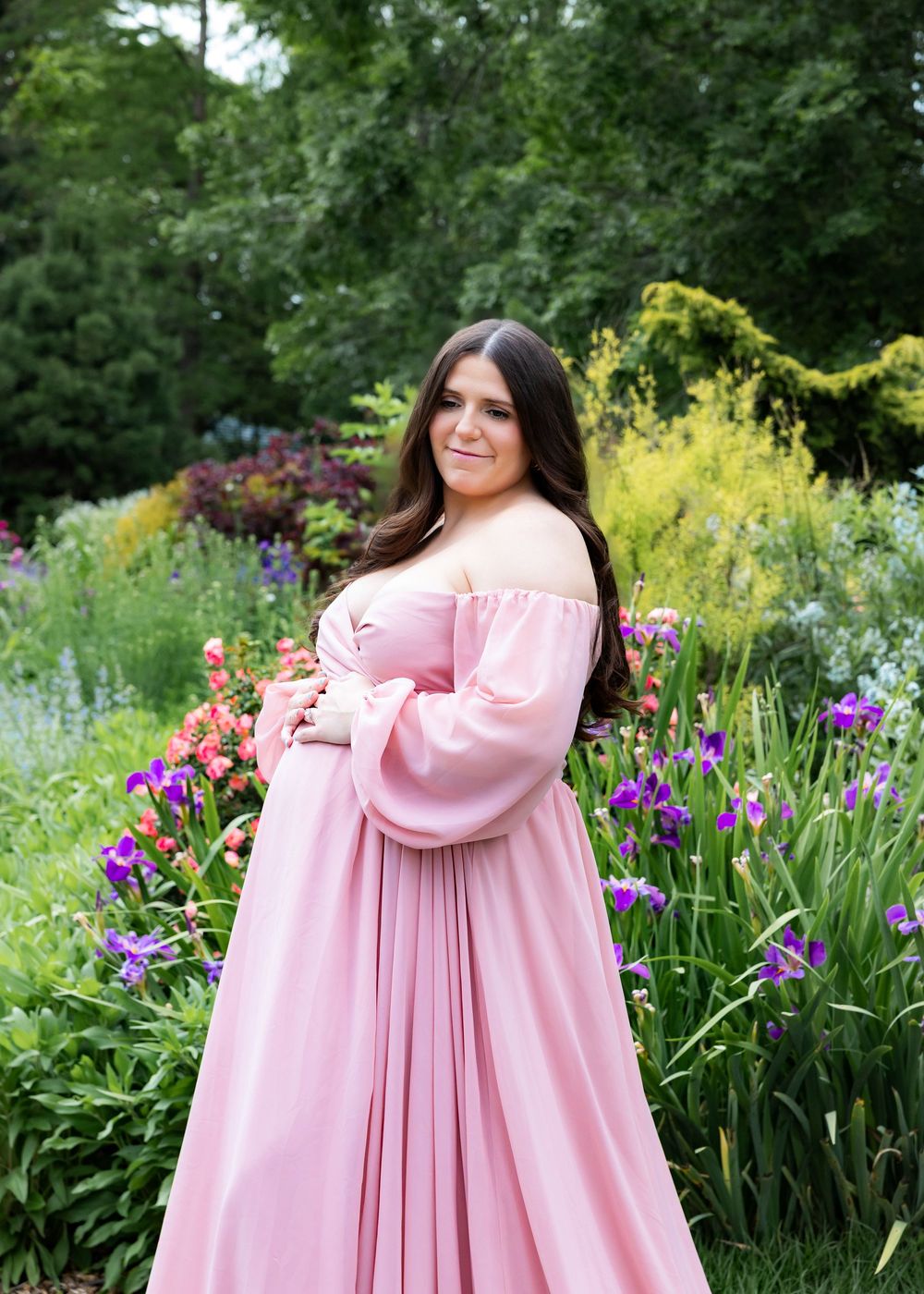 A person in a flowing pink dress twirls in a garden filled with vibrant purple iris flowers and yellow blooms.