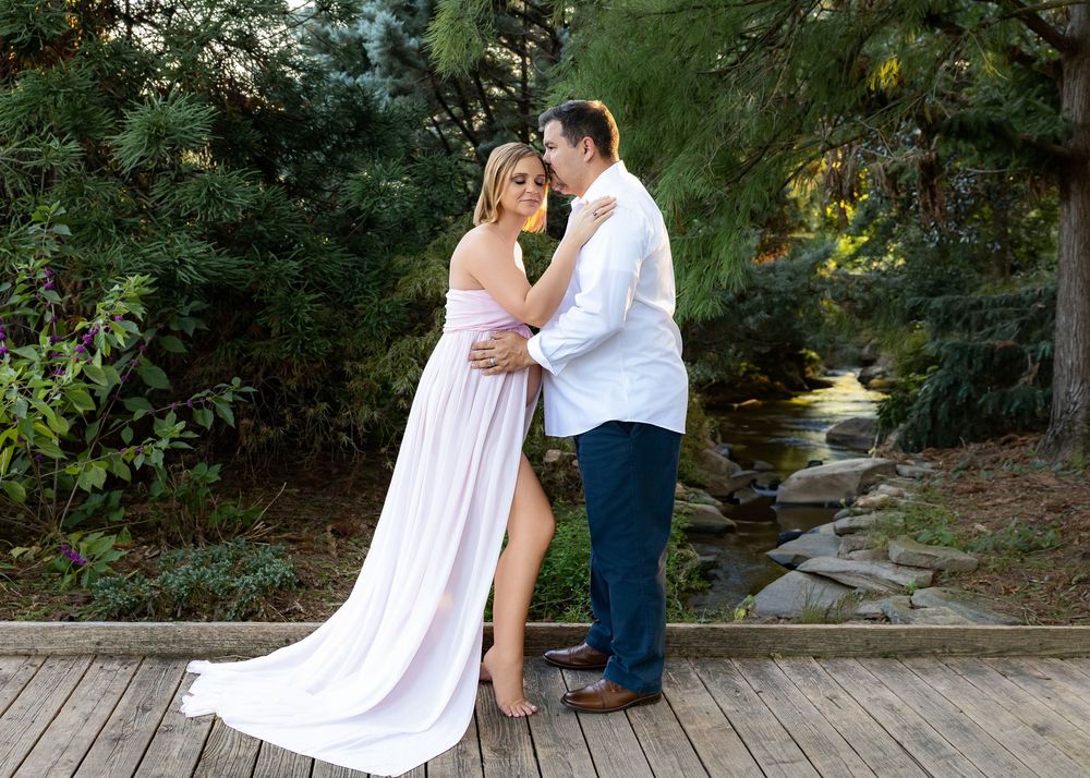 A couple shares a romantic moment on a rustic wooden deck surrounded by greenery during a maternity photo session.