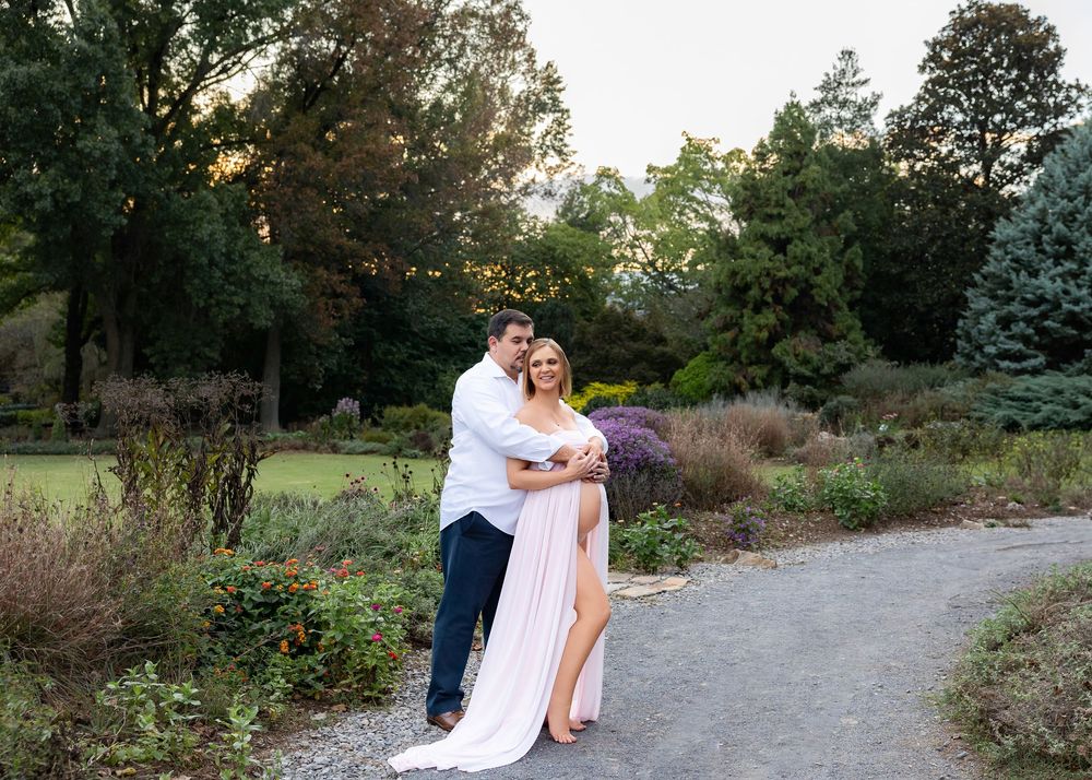 Maternity photoshoot share a romantic sunset moment along a winding garden path during a photo session.