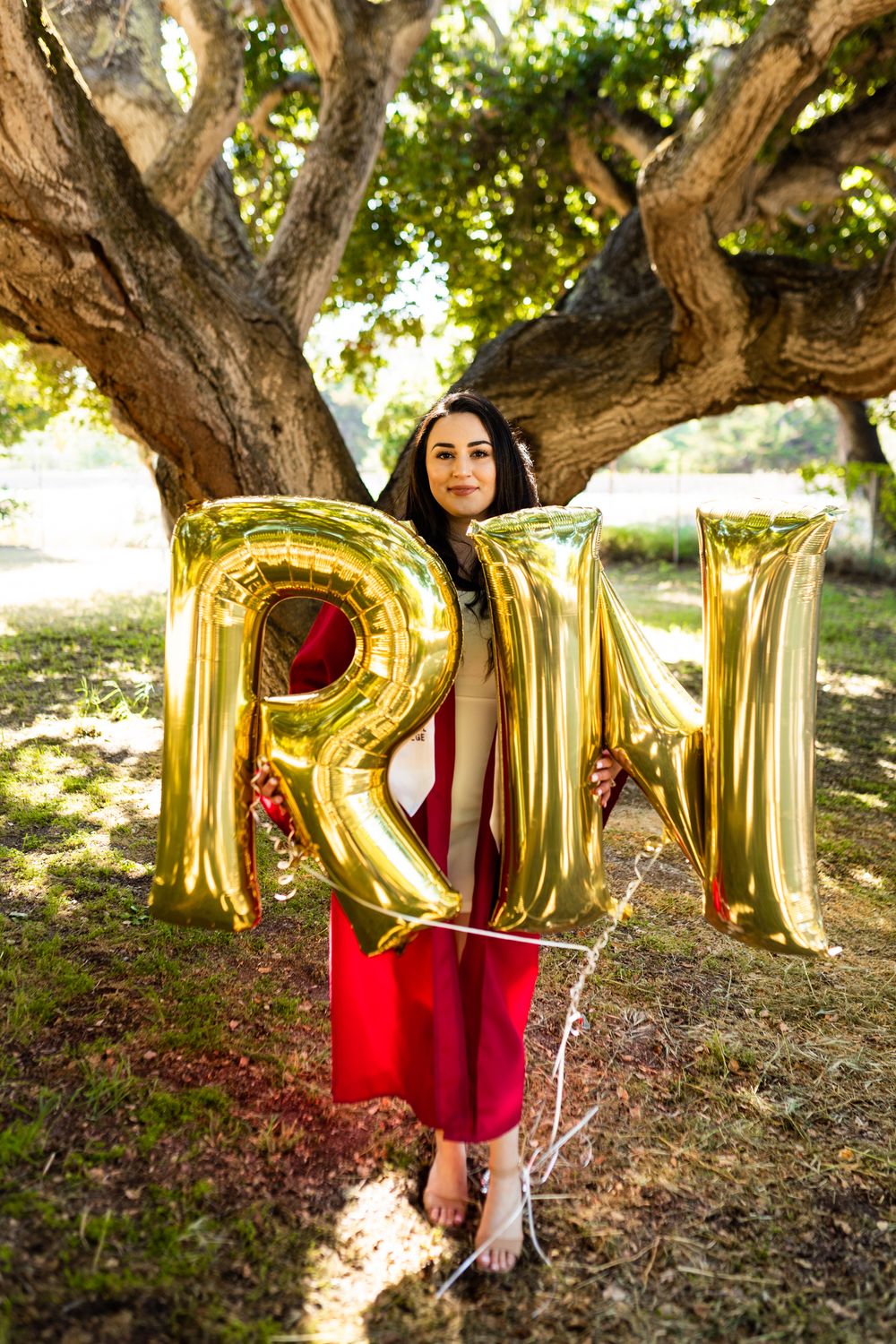 Gold balloon letters spell out a word against a tree trunk backdrop in a natural outdoor setting.