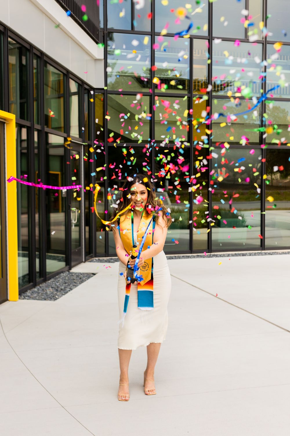 A sequence of images showing colorful confetti falling around a person in a white dress against a modern building exterior.