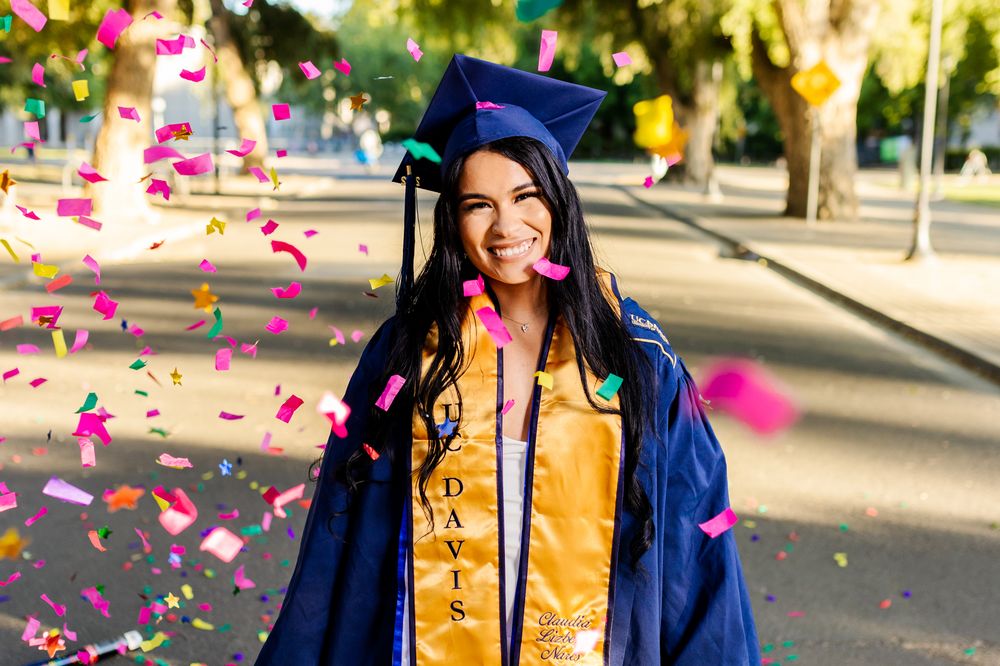 A graduation celebration with pink confetti falling in an outdoor setting on a sunny day.