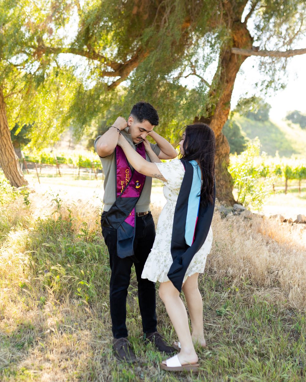 A couple poses playfully in a romantic outdoor photoshoot among trees and tall grass at sunset.