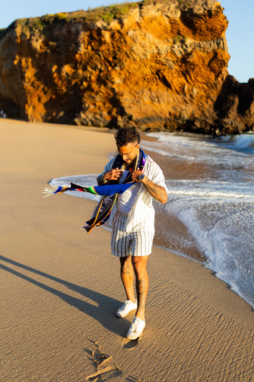 Person in white shirt and shorts plays along the beach shoreline at sunset with golden cliffs in background.
