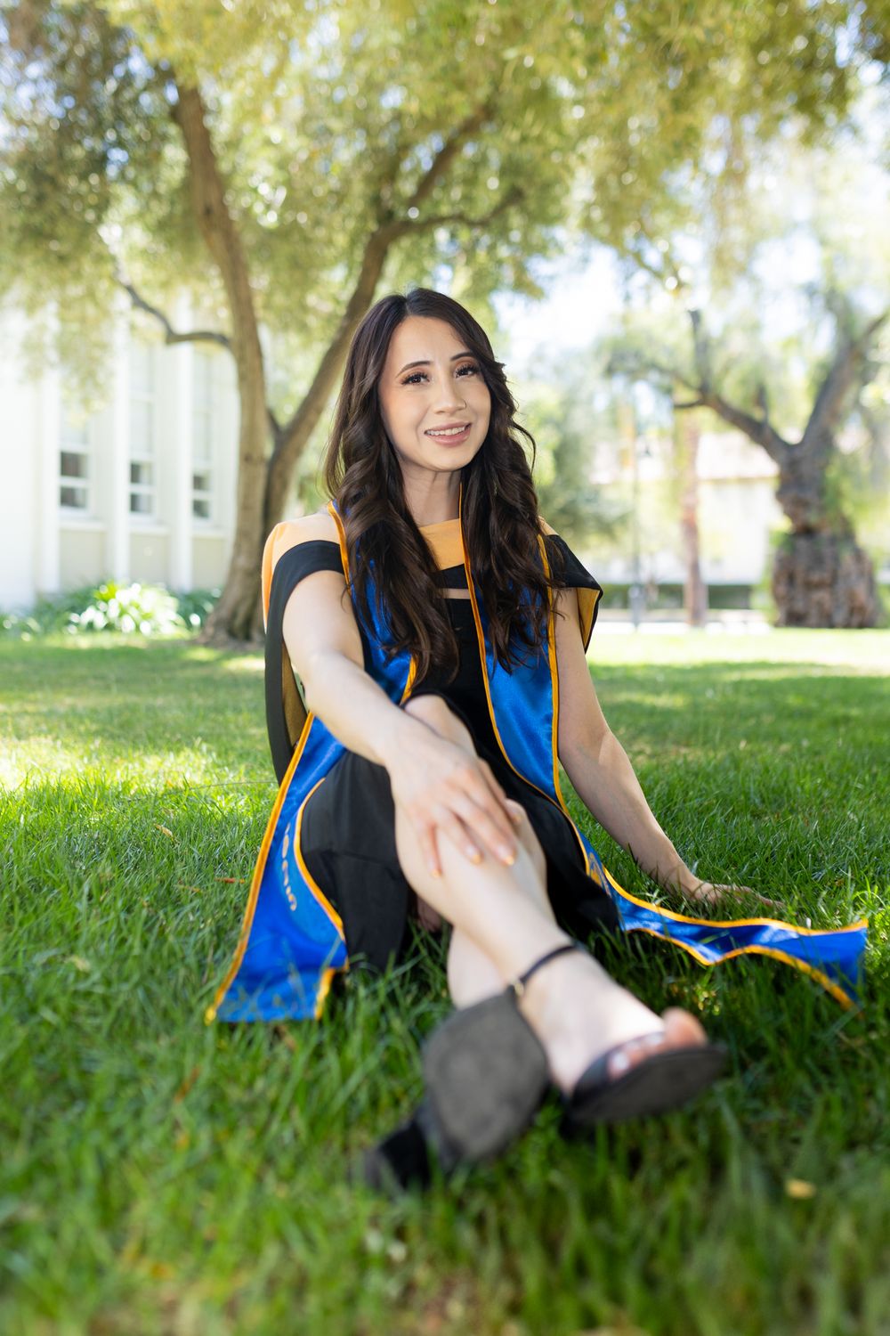 Woman in blue and black athletic wear stretches on grass under trees during outdoor workout session.