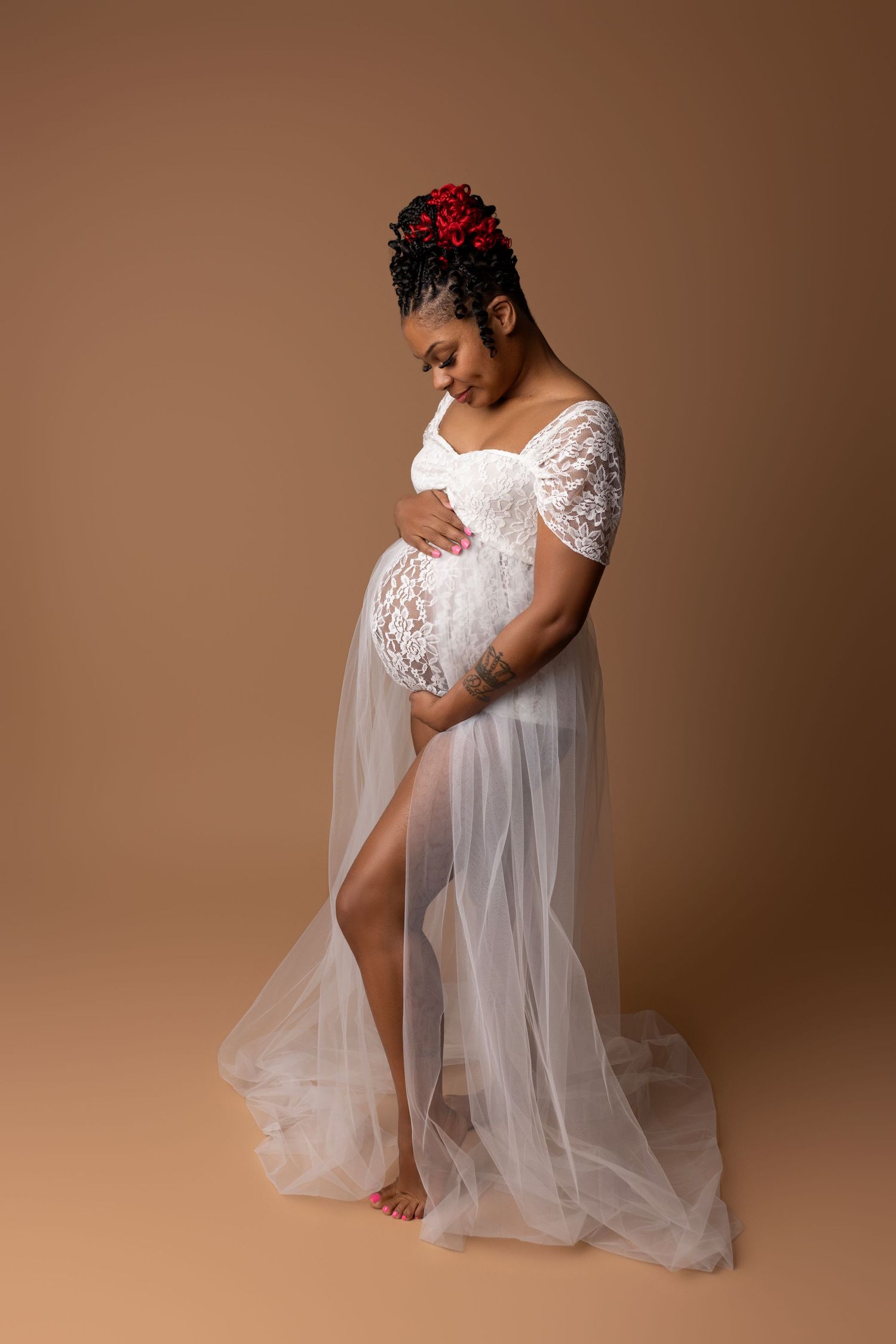 Pregnant woman gently cradling her baby bump in a white tulle and lace gown in Leander, TX photo studio