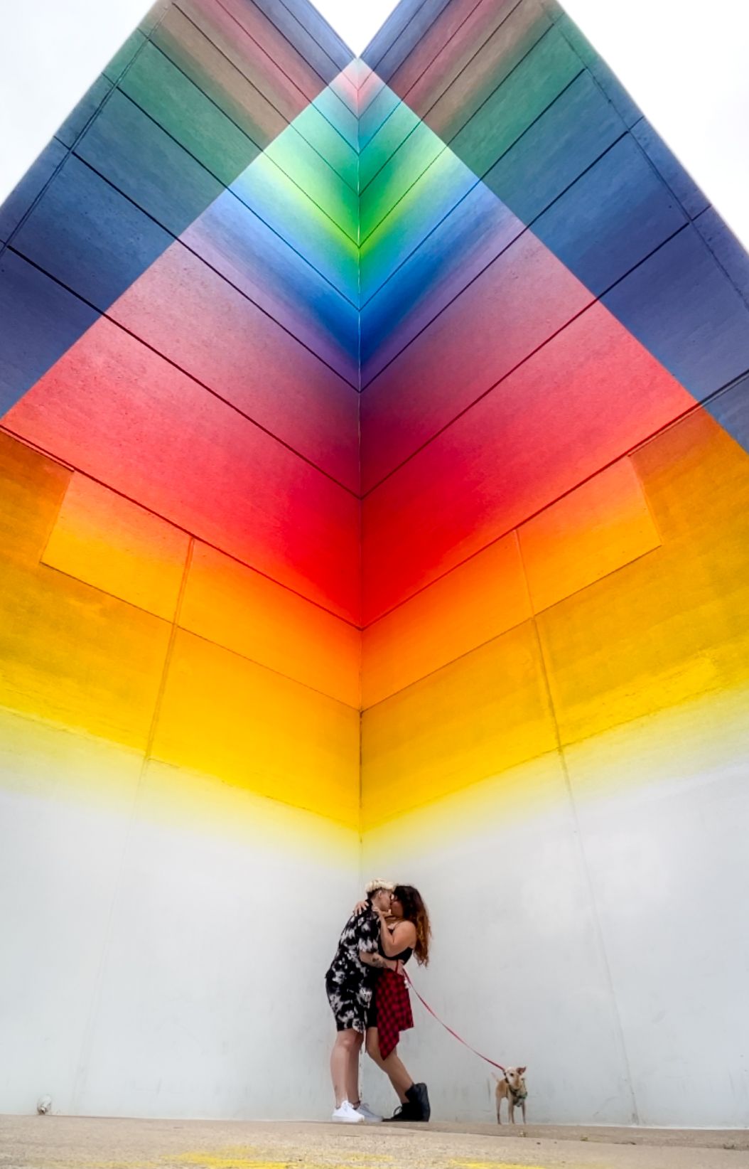 A colorful rainbow-painted geometric wall creates a striking backdrop in an urban setting.