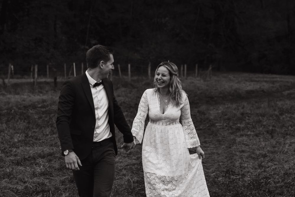 Black and white photo of newlyweds laughing together in rustic field.