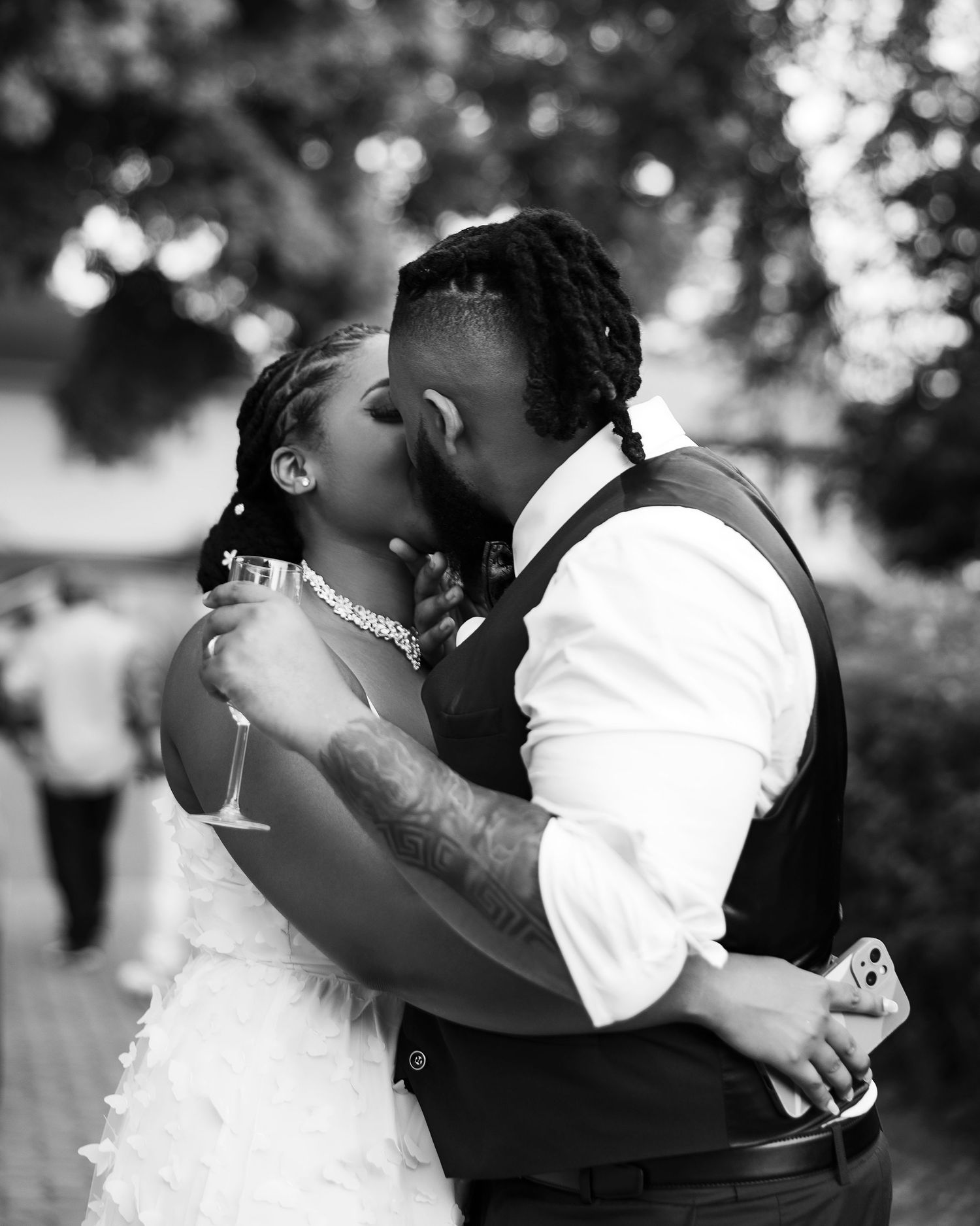 Black and white photo of a romantic wedding kiss outdoors with bokeh background.