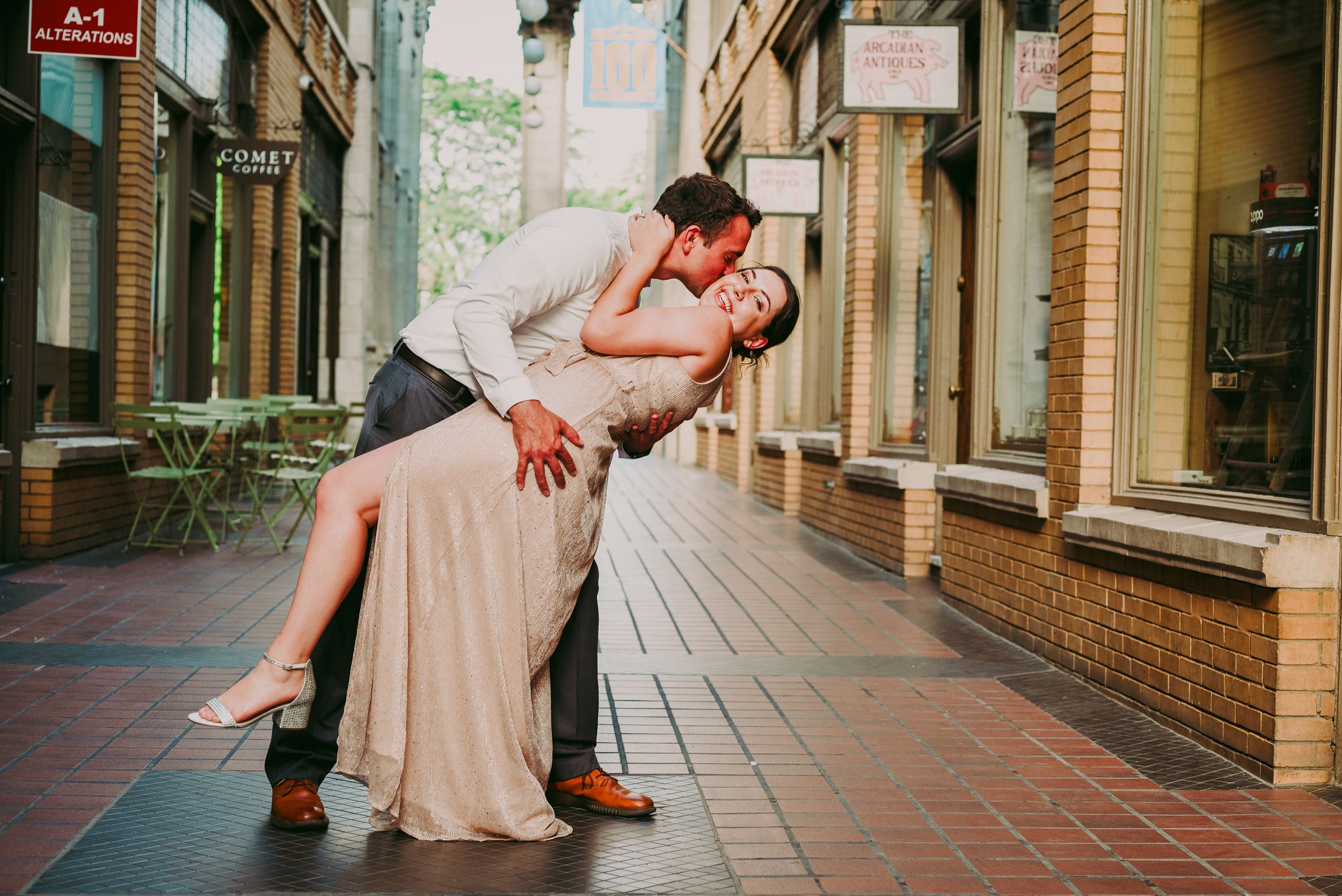 Couple sharing romantic dip kiss on a brick pedestrian street in urban setting.