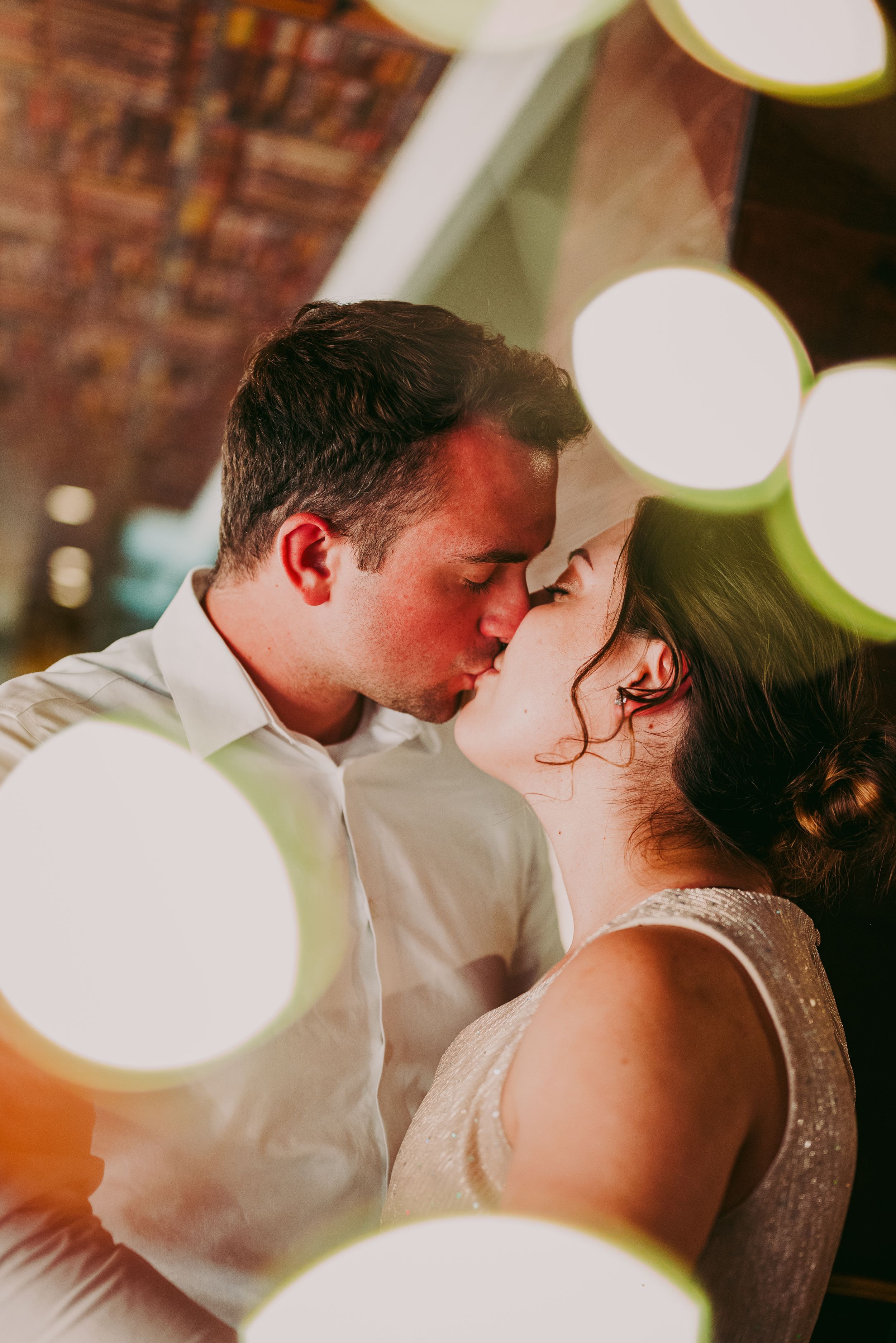 Couple sharing a tender kiss surrounded by soft bokeh lights in warm indoor setting.